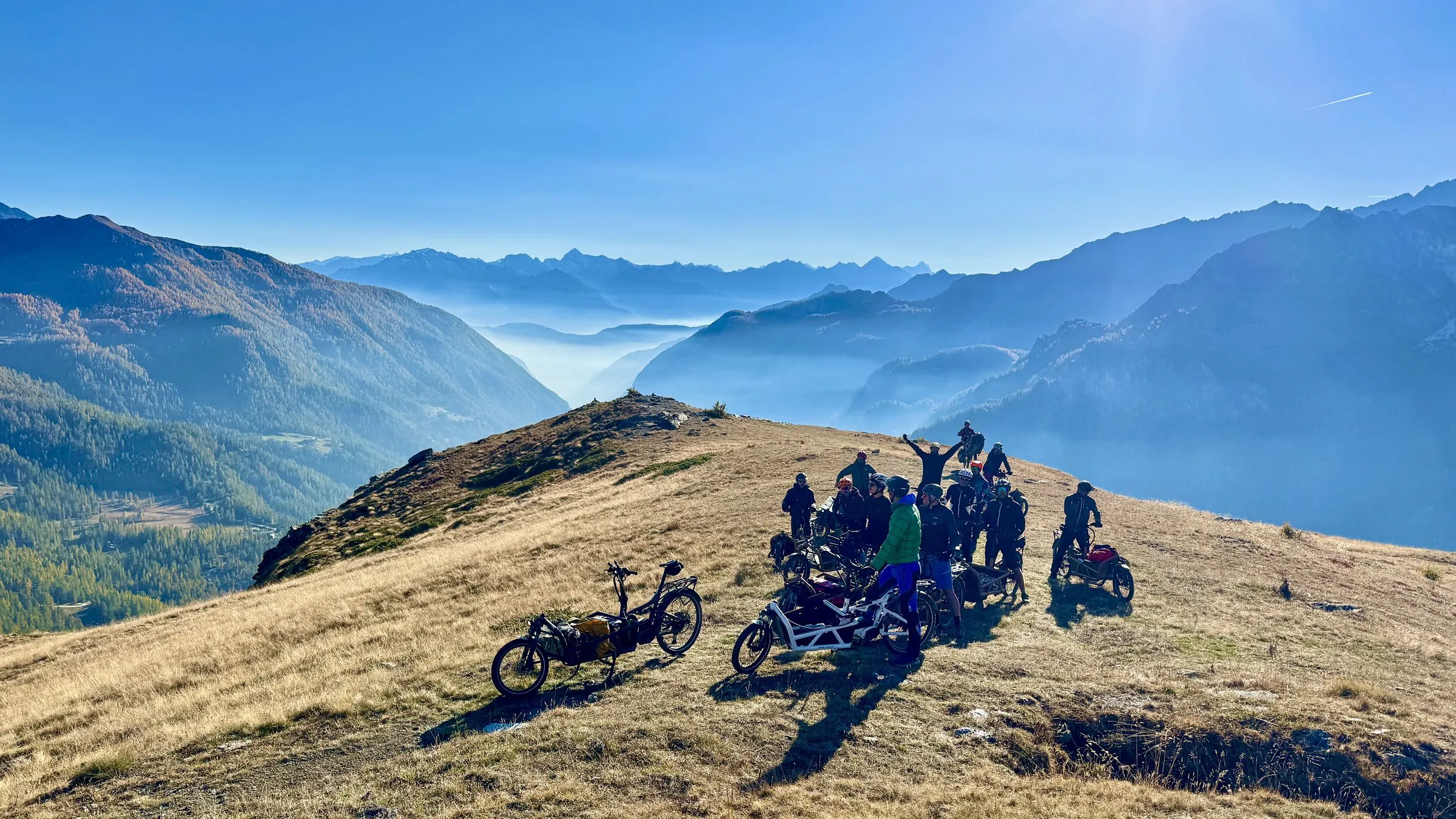 Il gruppo BigaAdventure in cargo bike su un crinale di montagna, con il mare di nebbia nella valle e le Alpi all'orizzonte